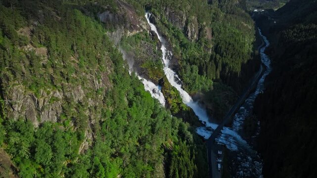 Latefossen cascading into deep forested valley in Norway. Wide aerial view highlighting steep rock walls, dense greenery, and dramatic mountain water flow.