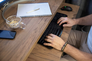 Hands on black computer keyboard at wooden desk