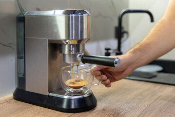 A silver espresso machine that pours coffee into a double-walled glass cup