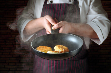 A chef works in a restaurant kitchen, flipping toasted buns in a frying pan. As dinner progresses, steam rises from the focused attention on the cooking process