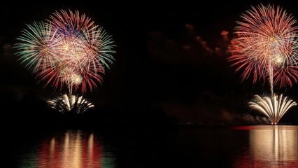 Spectacular nocturnal fireworks illuminating the dark sky, bursting in vibrant colors and casting brilliant reflections upon the calm water during a festive evening celebration