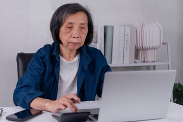 Serious senior Asian woman using calculator and laptop with worried expression. Elderly financial budget planning, stress from inflation, high cost of living, and retirement pension concept.