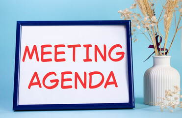 Meeting agenda symbol. Concept words Meeting agenda on beautiful wooden picture frame. Beautiful light blue background with flower vase. Business and Meeting agenda concept. Copy space.