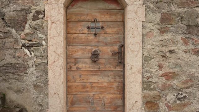 Antique wooden door in old stone building facade in Italy. Traditional architecture with metal handle, door knocker and small barred window. Historic medieval entrance or gate in village.