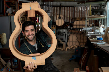 Smiling luthier holding guitar body mold in workshop, instrument maker portrait