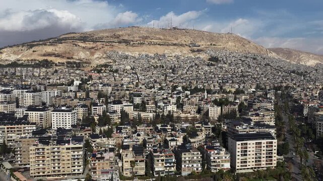 Aerial View of Syrian National Flag Waving on High Flagpole with Mount Qasioun and Damascus Cityscape in Background