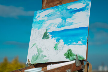 An easel holding a canvas displays a vibrant blue and green landscape painting under a bright sky.