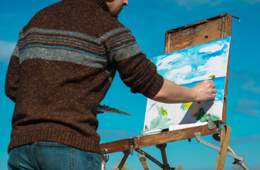 An artist painting a landscape on a canvas set on an easel outdoors, surrounded by nature.