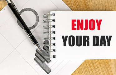 Notebook with text enjoy your day on desk with pen and printed charts