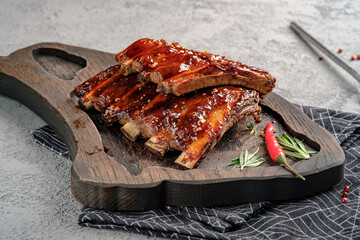 Sticky glazed pork ribs with barbecue sauce, garnished with fresh rosemary and red chili pepper on rustic wooden board. Juicy grilled spare ribs, delicious meat dish, gourmet barbecue style.