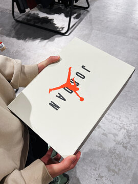 A person holds a white Nike Jordan sneaker box featuring the orange Jumpman logo in packaging