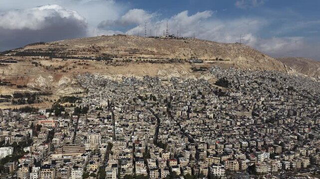 Aerial View of Syrian National Flag Waving on High Flagpole with Mount Qasioun and Damascus Cityscape in Background
