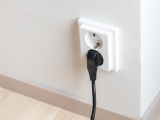 A close-up of a double electrical outlet mounted on a white wall, with a power cord plugged into one of the sockets. Mindful of electricity consumption and energy savings, managing electrical usage