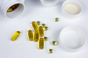 Omega-3 fatty acid dietary supplement capsules, along with vitamin D3 and K2, are scattered on white table near jars. Valuable marine fish oil in softgel capsules to increase Omega-3 level in body