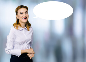 Portrait image of expressive emotional smile young business woman businesswoman in white shirt with empty mockup speech bubble. Happy cute girl against blurred modern office background