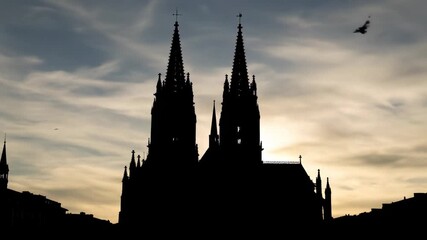Silhouette of a Gothic cathedral with twin spires at sunset.