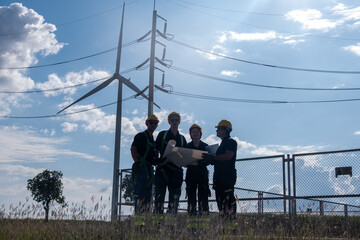 Group of workers examining plans near a wind turbine at a power station on a sunny day in an open field