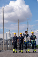 Four workers walk by a facility with tools in hand during a clear day in an industrial area under a blue sky