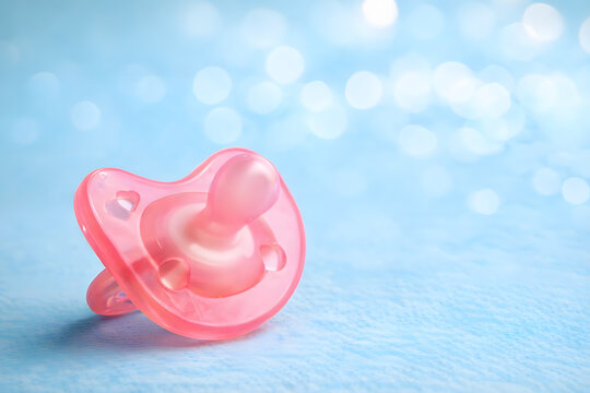 Pink pacifier on a soft blue background with bokeh lights representing infant care gentle parenting and baby product design