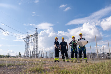 Workers stand at power station site with equipment near electric towers during day