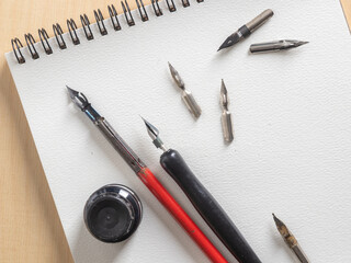 Collection of calligraphy dip pens with red and black holders and assorted metal nibs. Tools for lettering, artistic drawing, and creating varied line widths