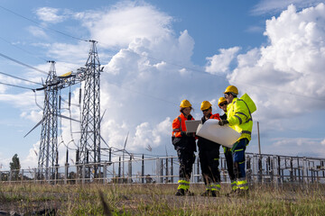 Team of workers discussing plans near power lines under cloudy sky in the daytime