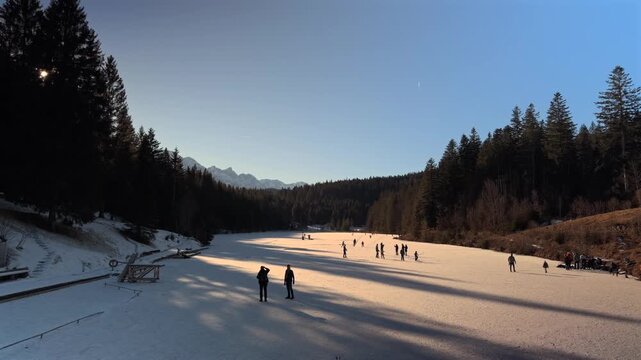 Lake Grubsee, Garmisch-Partenkirchen district, Upper Bavaria, Germany. People ice skating onfrozen Grubsee lake near Kruen. Authentic winter sport scene in Bavarian Alps. Skating on the natural ice