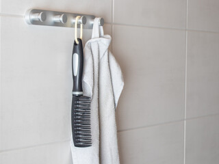 Wall-mounted metal hook rack in a tiled bathroom. Black comb with white handle and loop, light grey hand towel, bright modern setting with large square tiles