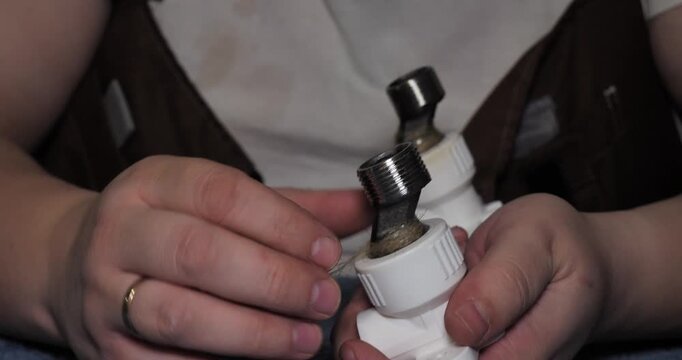 Professional plumber's hands carefully wrapping sealant tape around the threads of a plastic and metal pipe fitting before installation to ensure a watertight connection for plumbing repair.