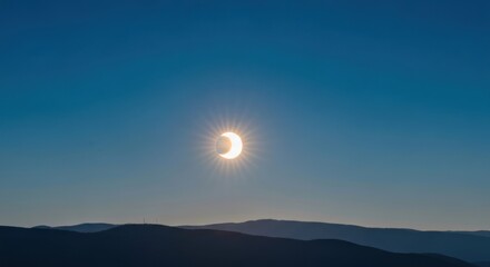 Crescent sun eclipsed, shining in a deep blue sky over shadowed hills