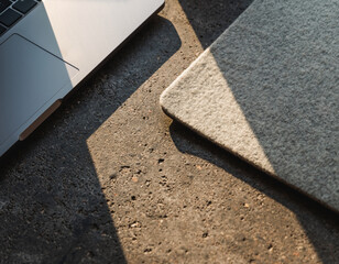 Minimal modern office background with laptop on rough concrete surface. warm sunlight creates deep shadow and highlights texture of material for peaceful, focused mood