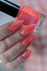 Woman hand with long nails and light orange coral neon manicure holds