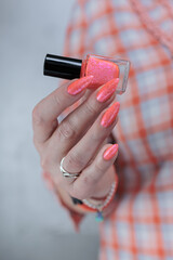 Woman hand with long nails and light orange coral neon manicure holds
