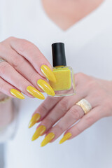 Female hand with long nails and a bottle of bright yellow orange nail polish	