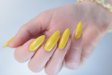 Female hand with long nails and a bottle of bright yellow orange nail polish	
