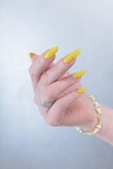 Female hand with long nails and a bottle of bright yellow orange nail polish	