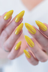 Female hand with long nails and a bottle of bright yellow orange nail polish	