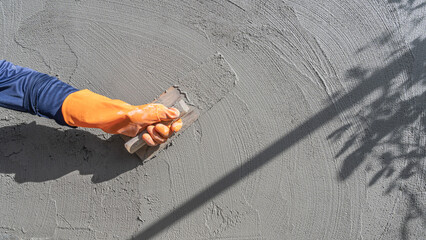 Hand worker plastering with holding trowel handle polished wet grey cement plaster wall background well rough concrete free space and shadow light for text presentation