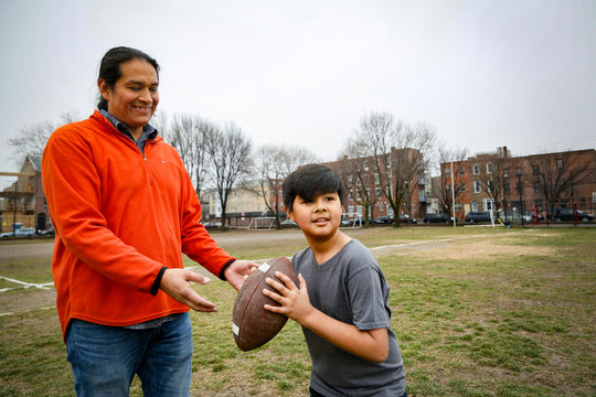 Philadelphia, Pennsylvania, USA. Native American father teaching his young son how to throw a football