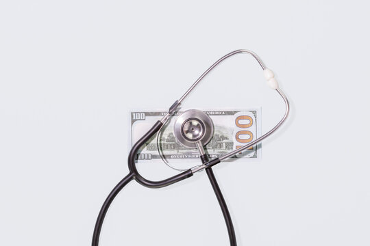 Stethoscope Lying on One Hundred Dollar Bill over Plain Light Blue Background. Conceptual Visual for Healthcare Costs, Medical Insurance Expenses, Paid Medicine and Economic Aspects of Health Services - Powered by Adobe