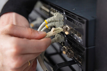 Adult woman technician connects network cables to server hardware in a data center for maintenance and security checks