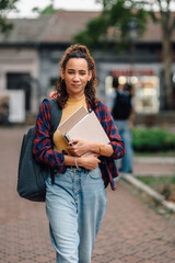 University student walking on campus holding books and laptop