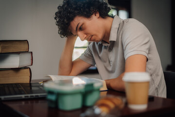 Focused student studying with laptop and books, enjoying coffee and croissant