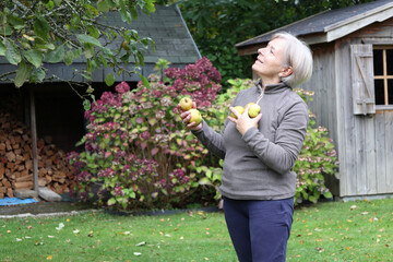Senior woman rejoices at the apple harvest in her garden