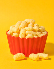 Puffed Corn Snacks in Red Bowl on Bright Yellow Background

