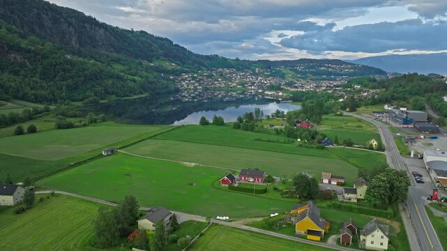 Rural landscape near Steinsdalsfossen waterfall in Norheimsund, Norway. Wide aerial view of green farmland, small homes, and calm water surrounded by forested hills.