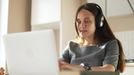 Working on laptop with headset young woman typing on laptop in home office showing concentration during remote online study or work for student or freelancer focused on computer and meeting session - Powered by Adobe