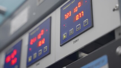 Close-up of an industrial control panel with illuminated digital displays and status icons, showing real-time measurements and system parameters in a manufacturing or laboratory setting. - Powered by Adobe