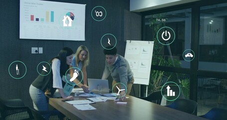 Reviewing three colleagues wearing business casual leaning over laptop and display in meeting room