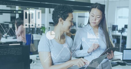 Pointing two women in blue blouse and grey top reviewing tablet in open-plan office, HUD overlays